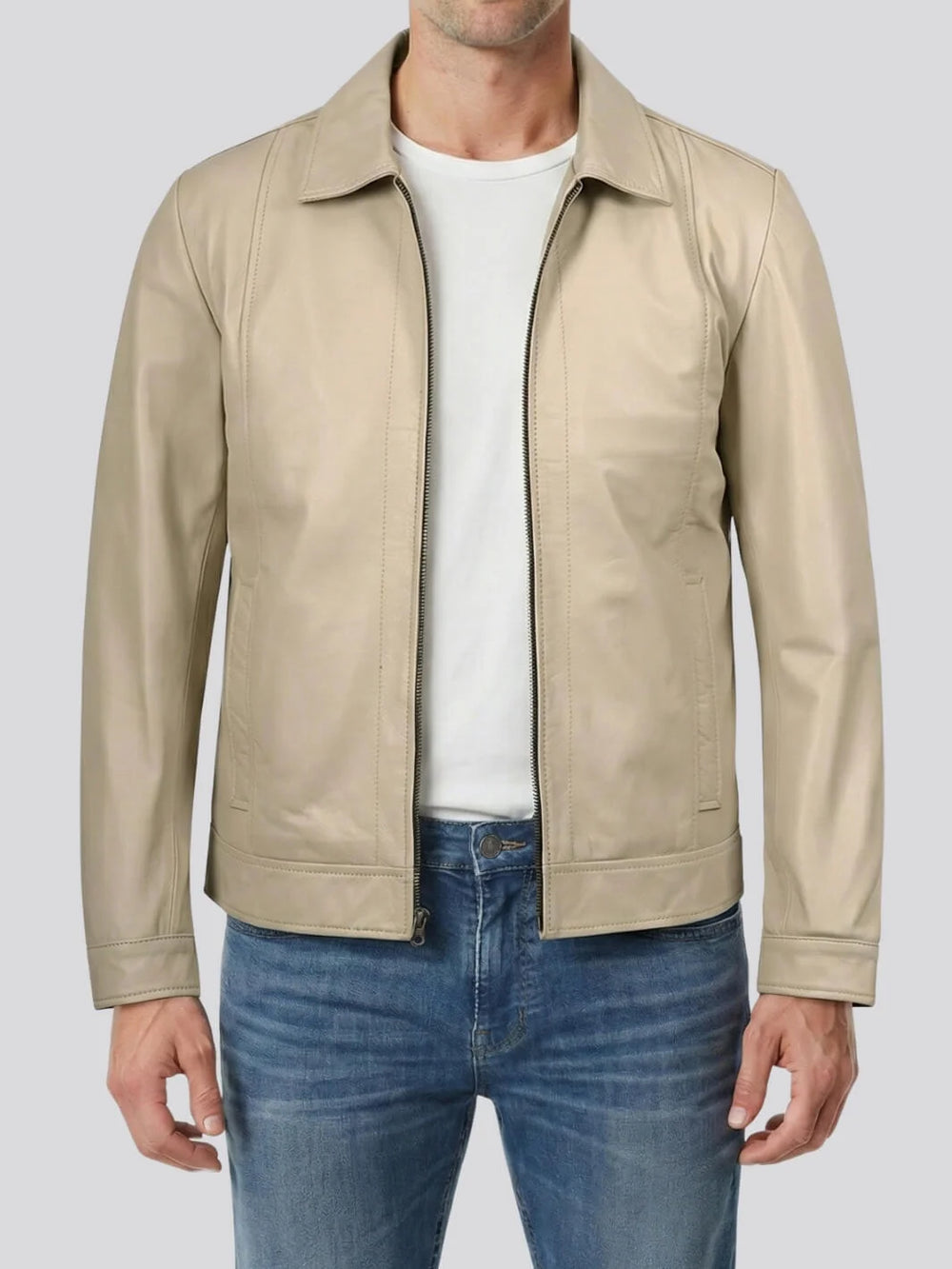 Man wearing a beige leather jacket over a white shirt and blue jeans on a light gray background